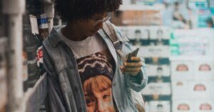 Mulher segurando o celular no supermercado. (Foto: Pexels)