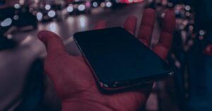 Mão segurando o celular no meio da rua. (Foto; Pexels)