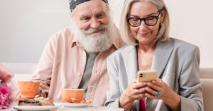 Casal de idosos feliz usando o celular. (Foto: Pexels)