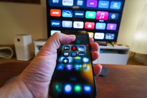 Close-up of a hand holding a phone displaying streaming apps in front of a TV with multiple app icons. Netflix